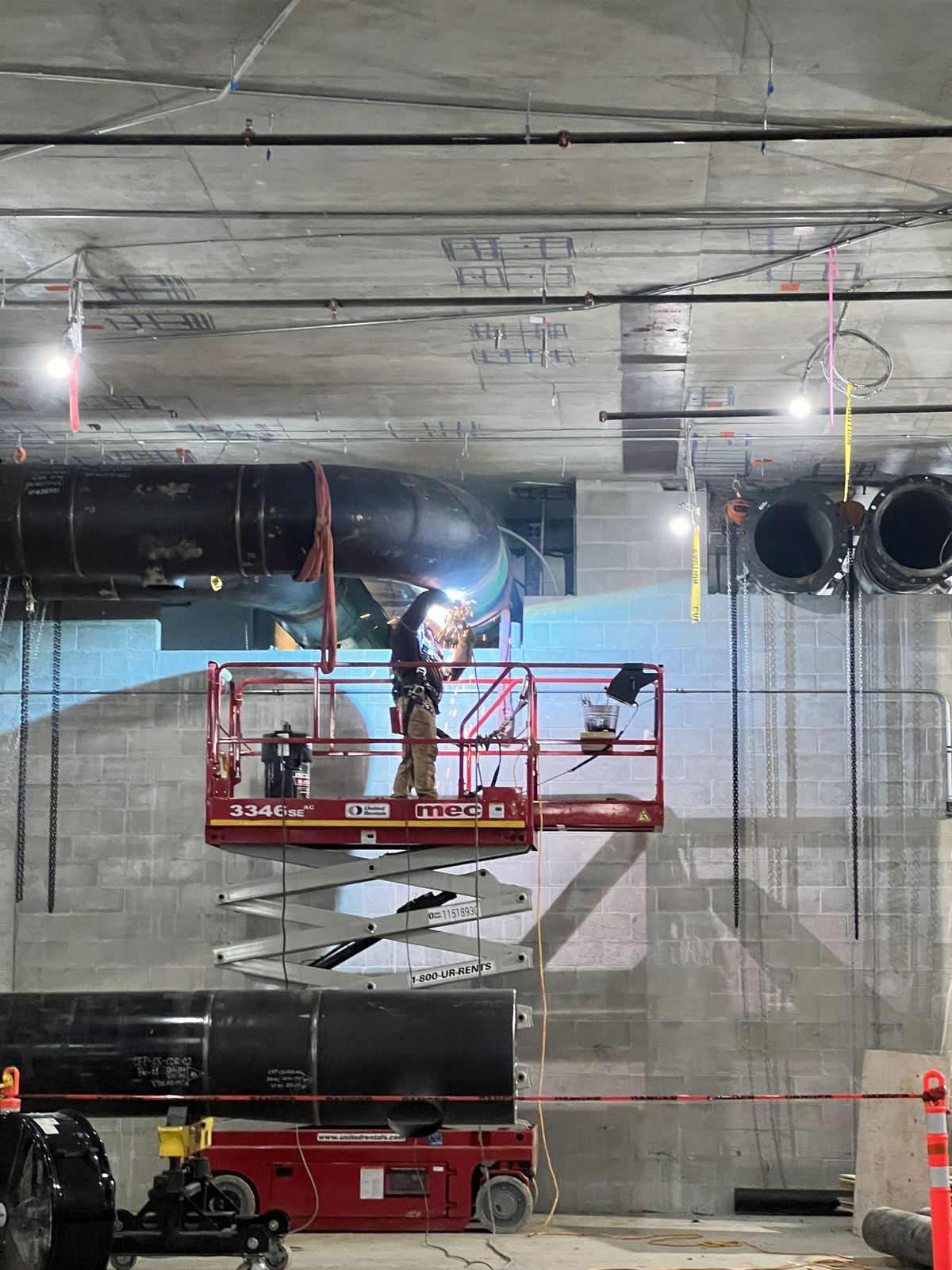 Welder on a scissor lift welding large-diameter pressure pipe at a commercial site