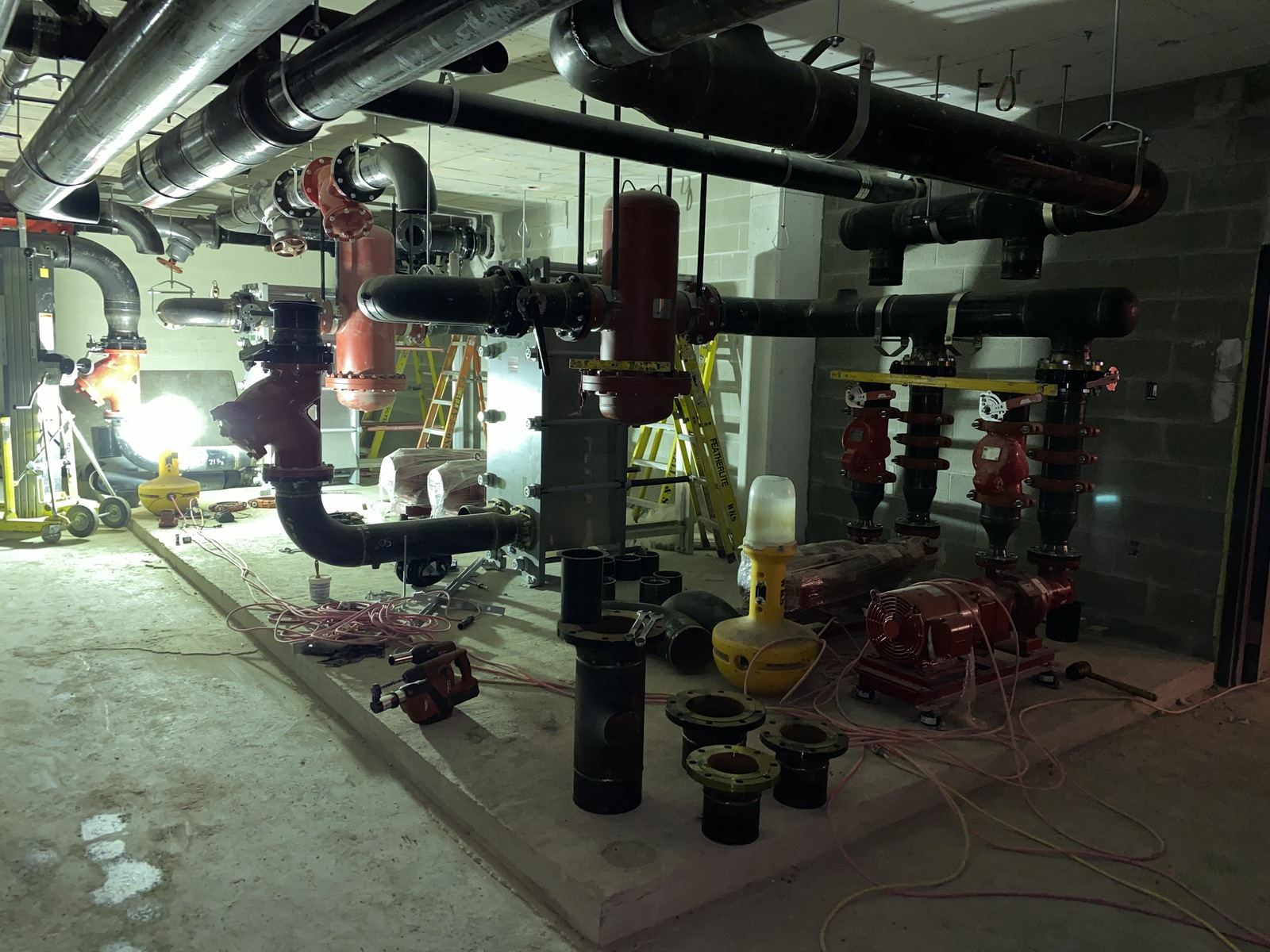 Commercial mechanical room with black and red pipework, pumps and valves under work lights
