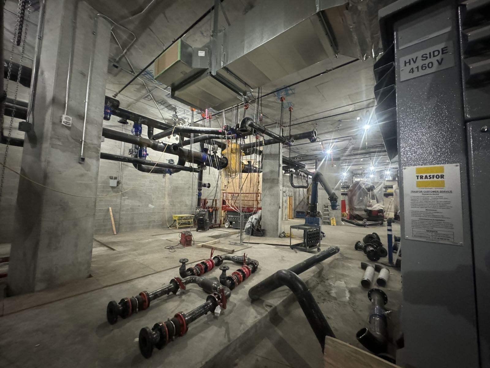 Underground mechanical room with black pipe runs and flanged pipe spools on the floor