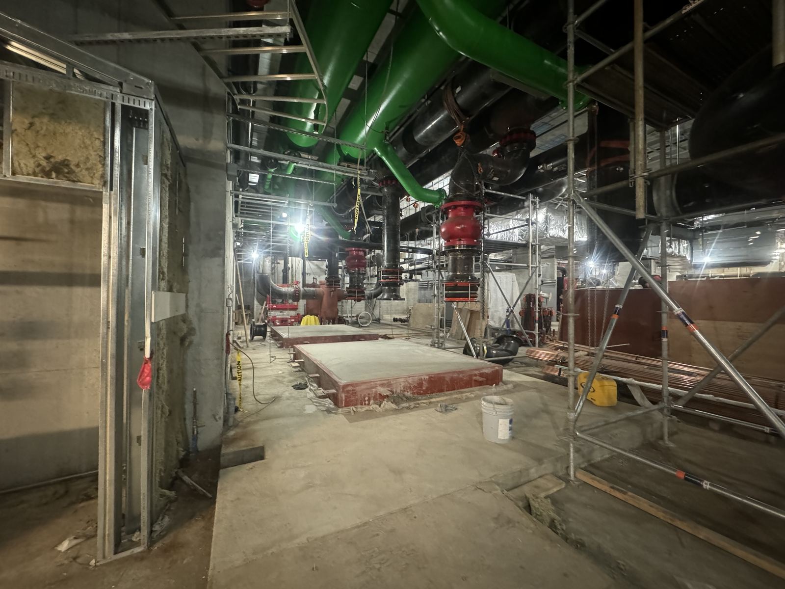 Mechanical space with large green pipes, red fittings, and scaffolding