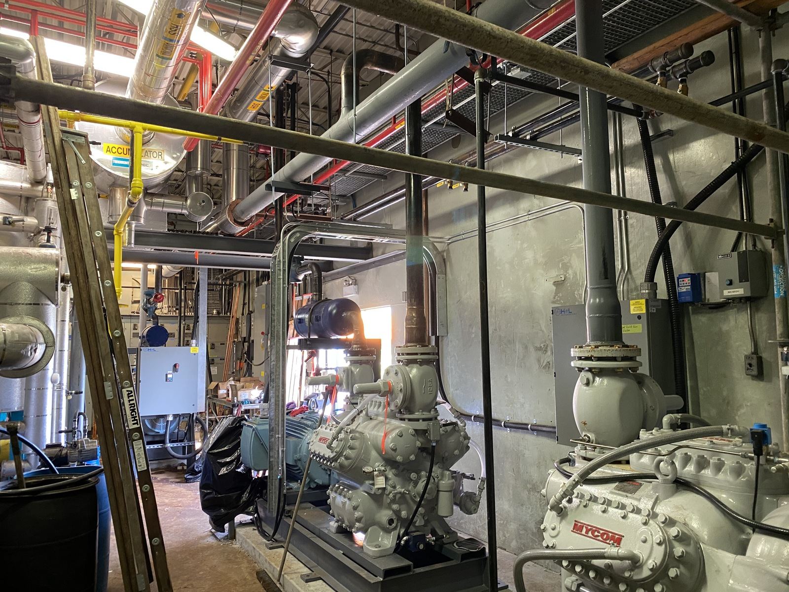 Industrial plant room with large compressors, overhead piping and valves