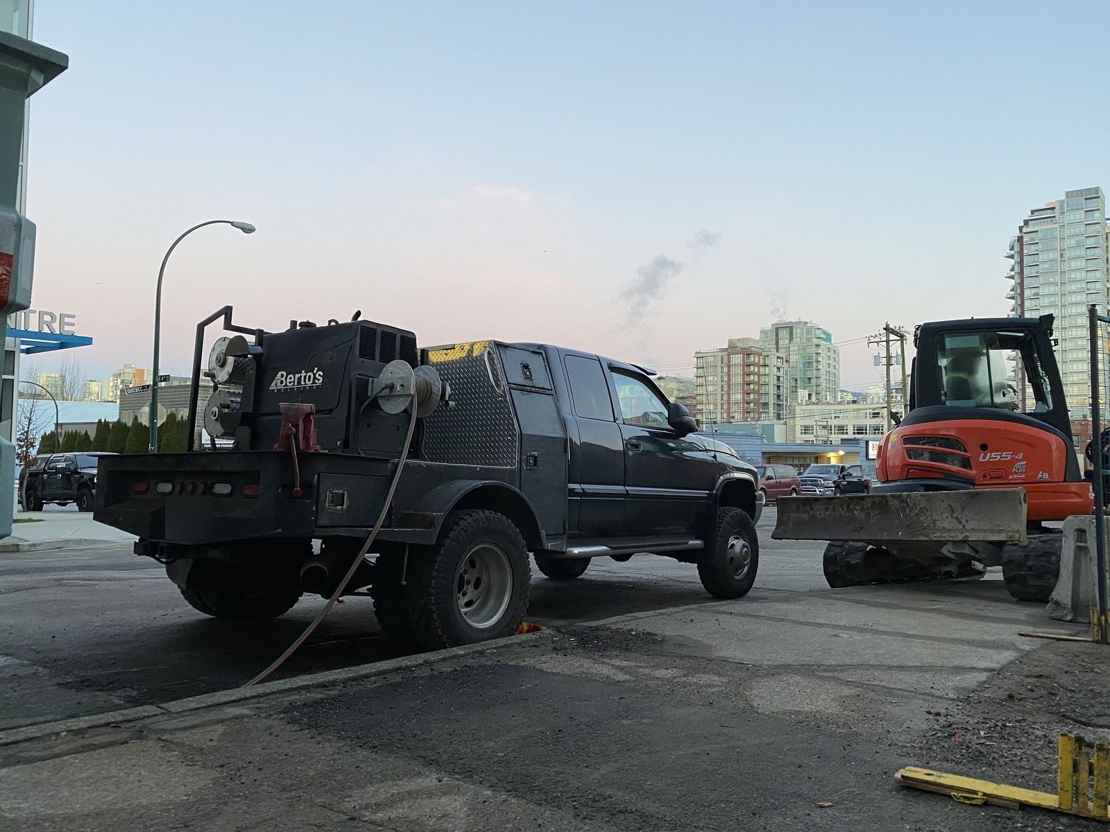 Berto's mobile welding truck parked beside an excavator at a city construction site at dusk
