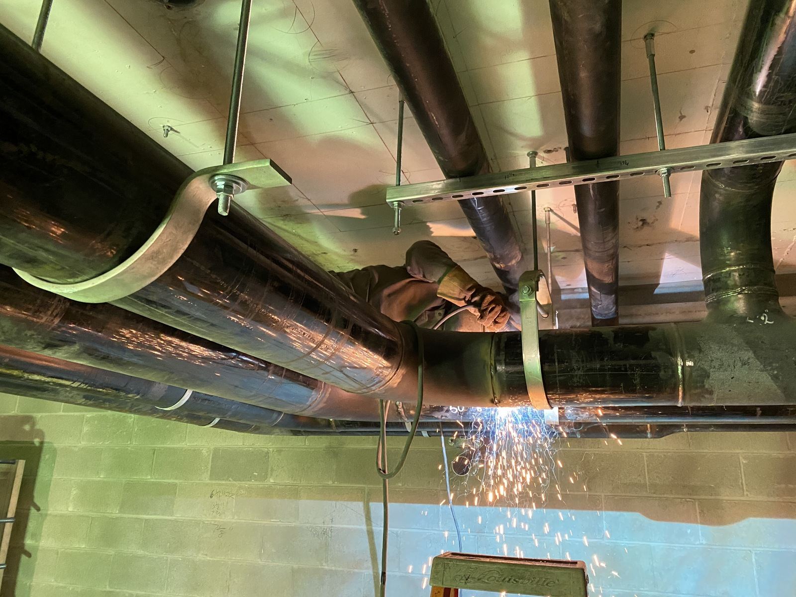 Welder working overhead on pipe in a parkade ceiling with sparks falling
