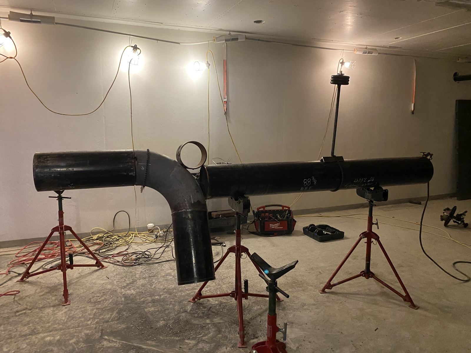 Black steel pipe spool with a tee set up on red pipe stands, ready for welding