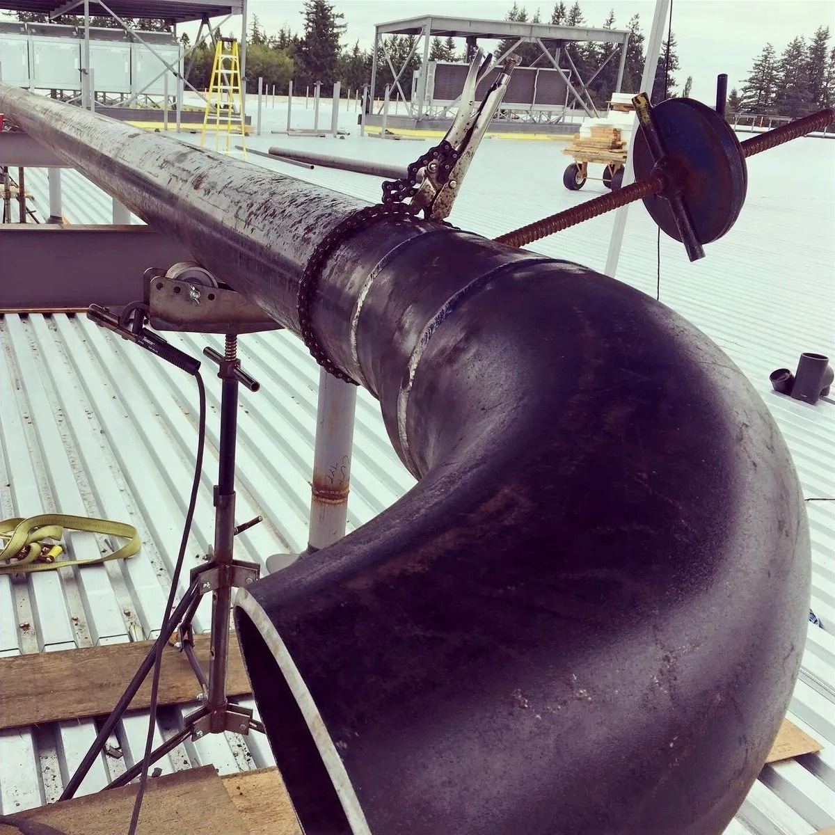 Large black steel pipe elbow on a rooftop installation under a clear sky