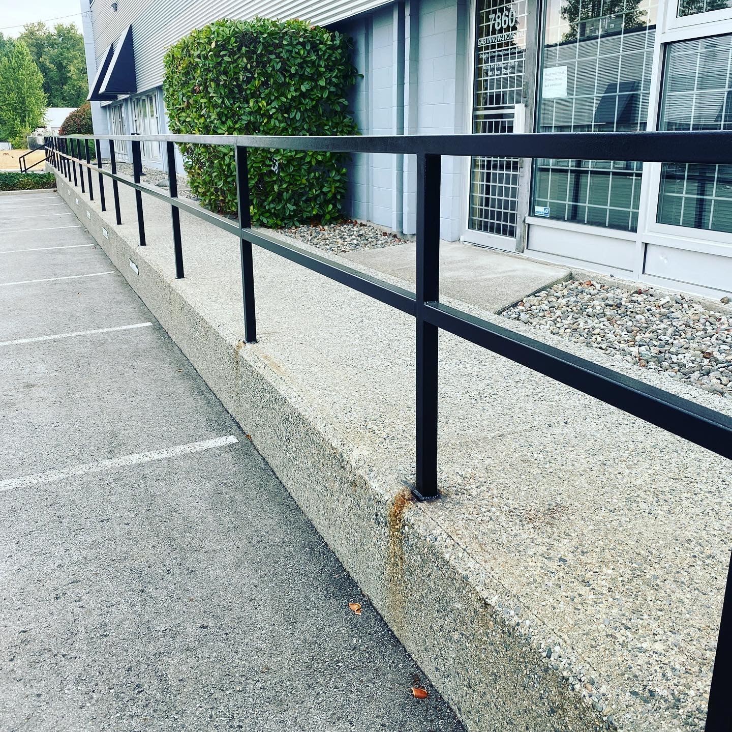 Black steel handrail running along a concrete ramp beside a commercial building