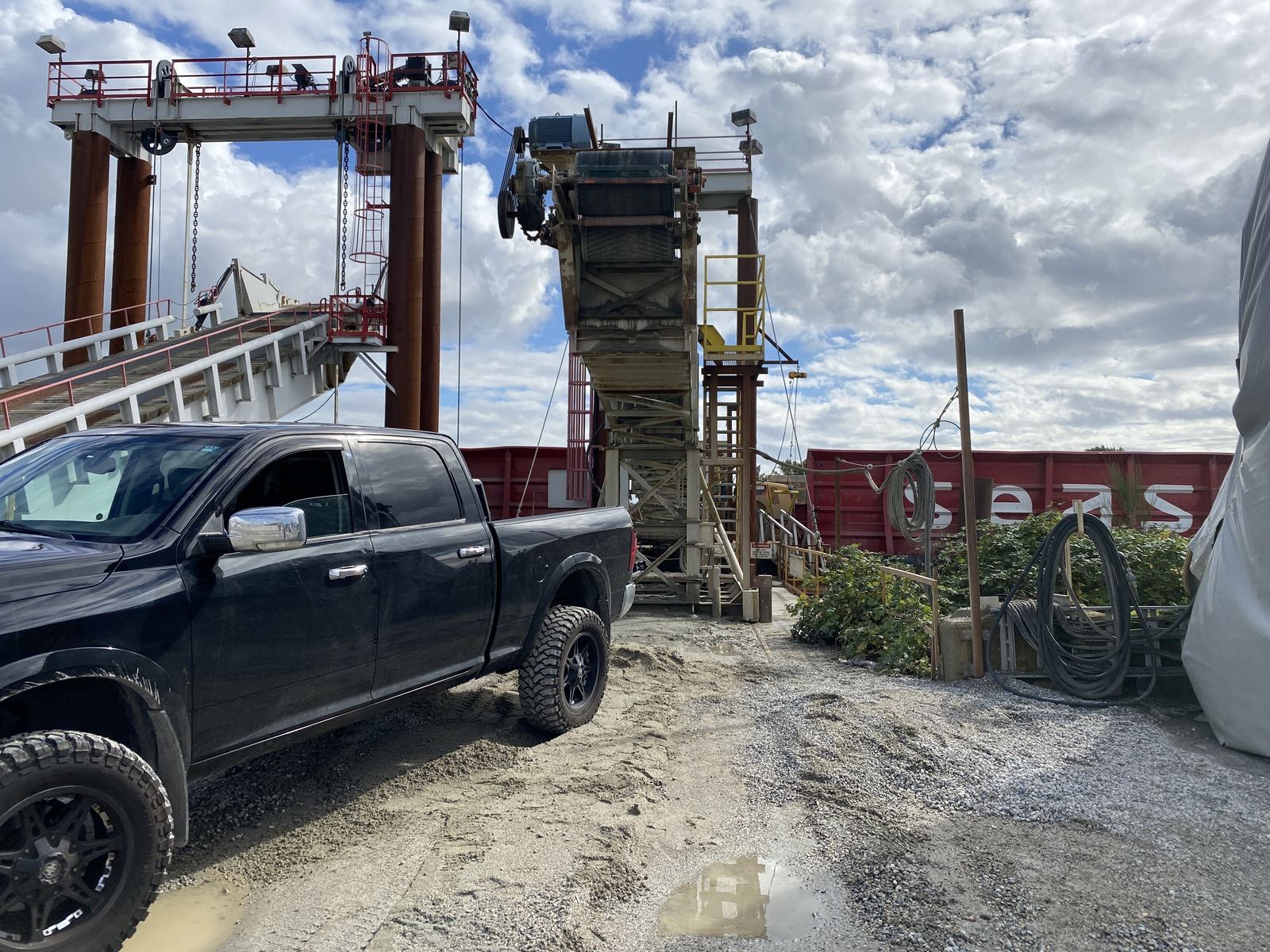 Pickup truck parked at a waterfront industrial site beside a barge ramp and conveyor