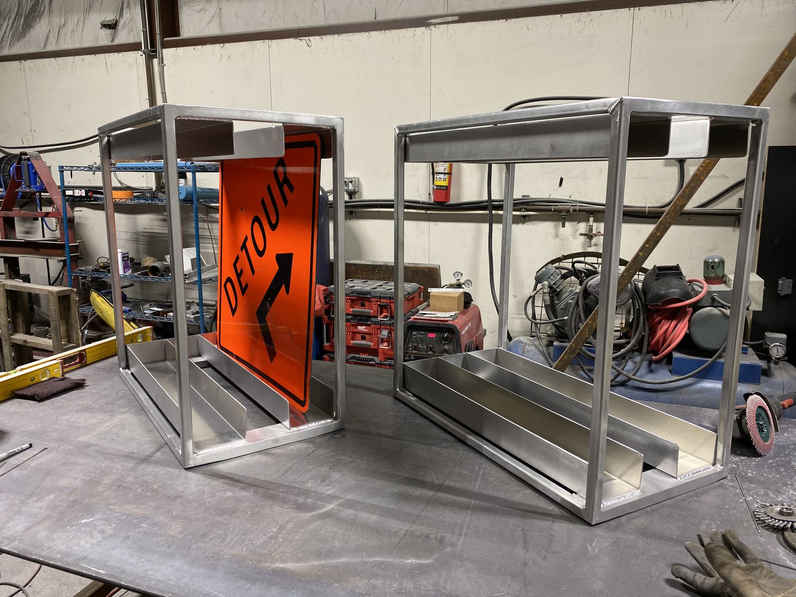 Two fabricated aluminum sign stands in the shop, one holding an orange detour sign