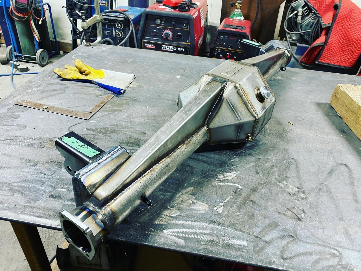 Fabricated stainless steel assembly on a welding table, welding machines in the background