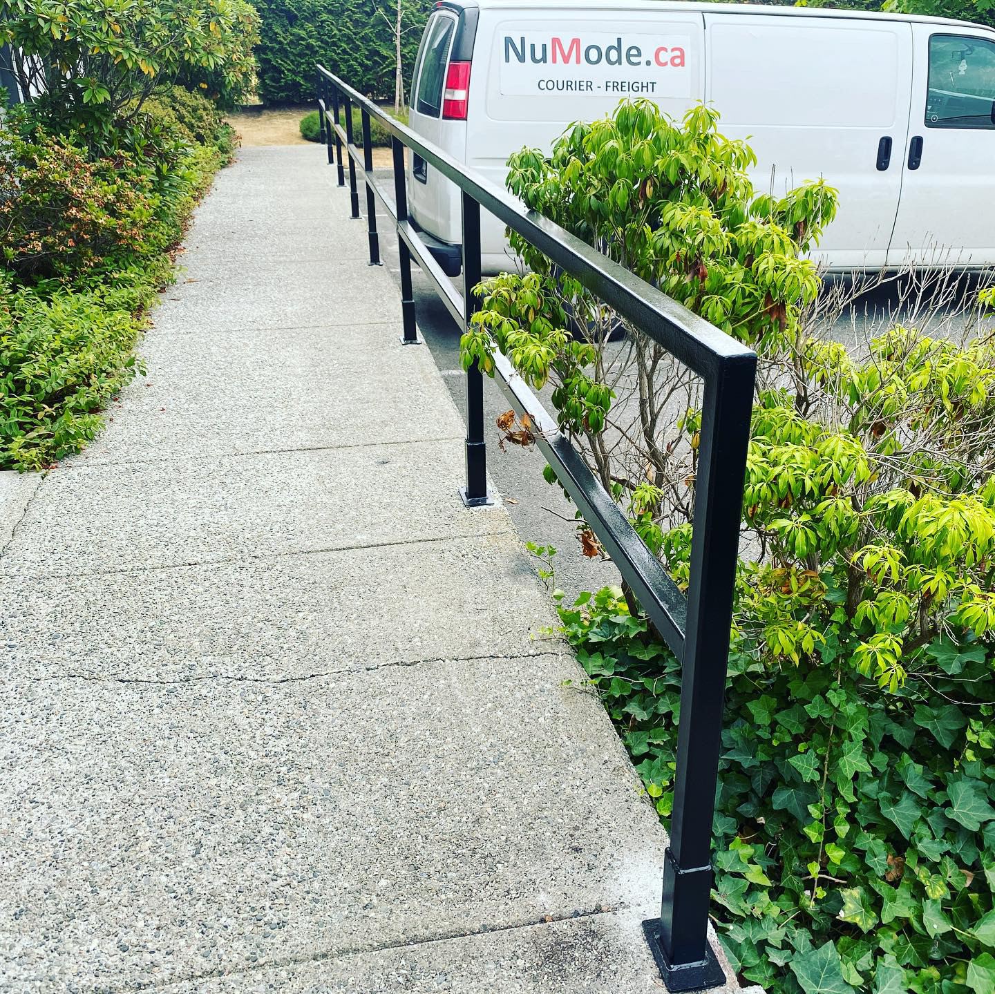 Black steel handrail along a landscaped concrete walkway