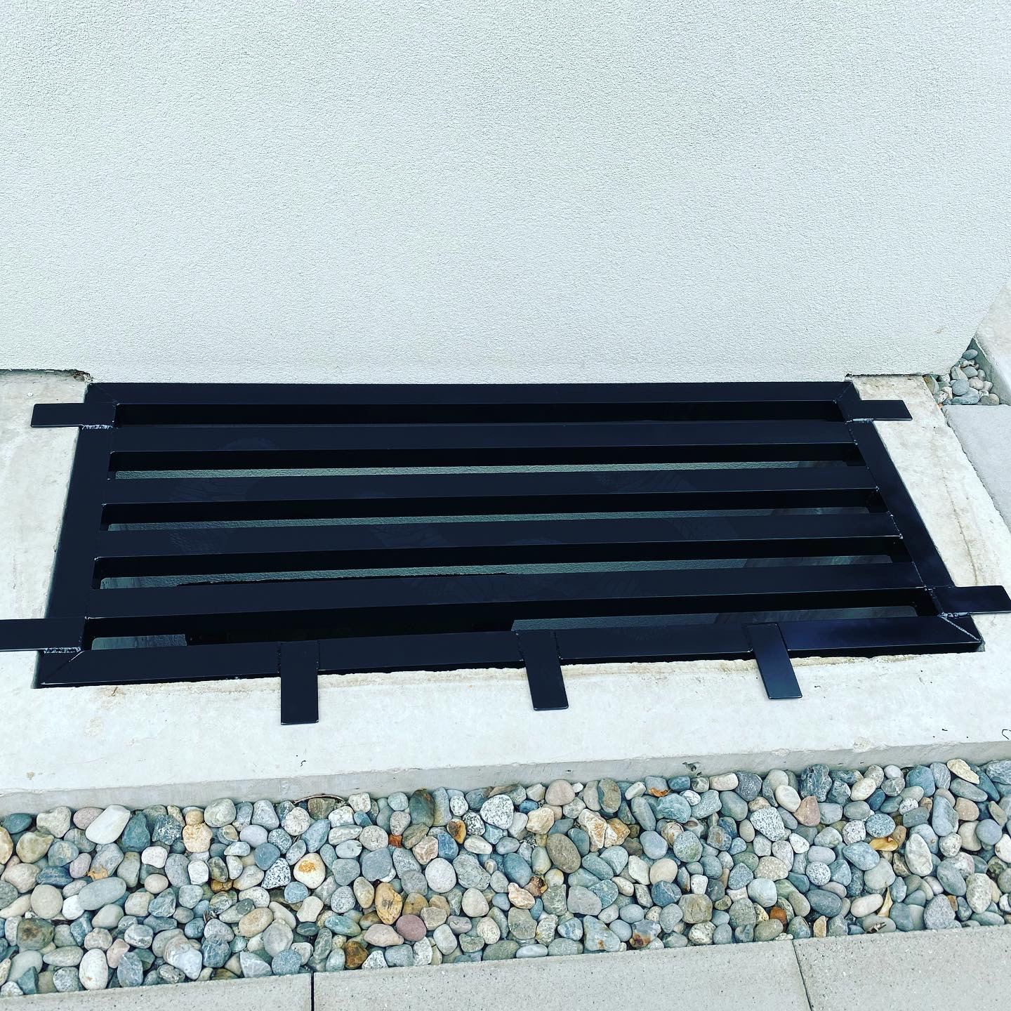 Black steel grate set into a concrete surround above a bed of river rock