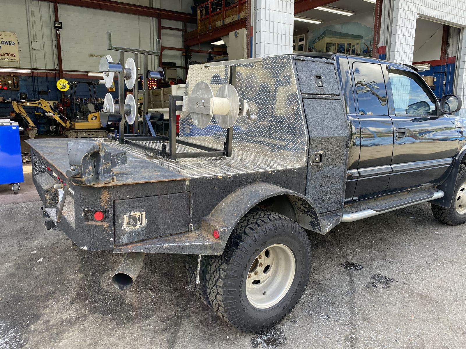Side view of the welding truck outside a shop, showing diamond-plate tool boxes and the reel rack