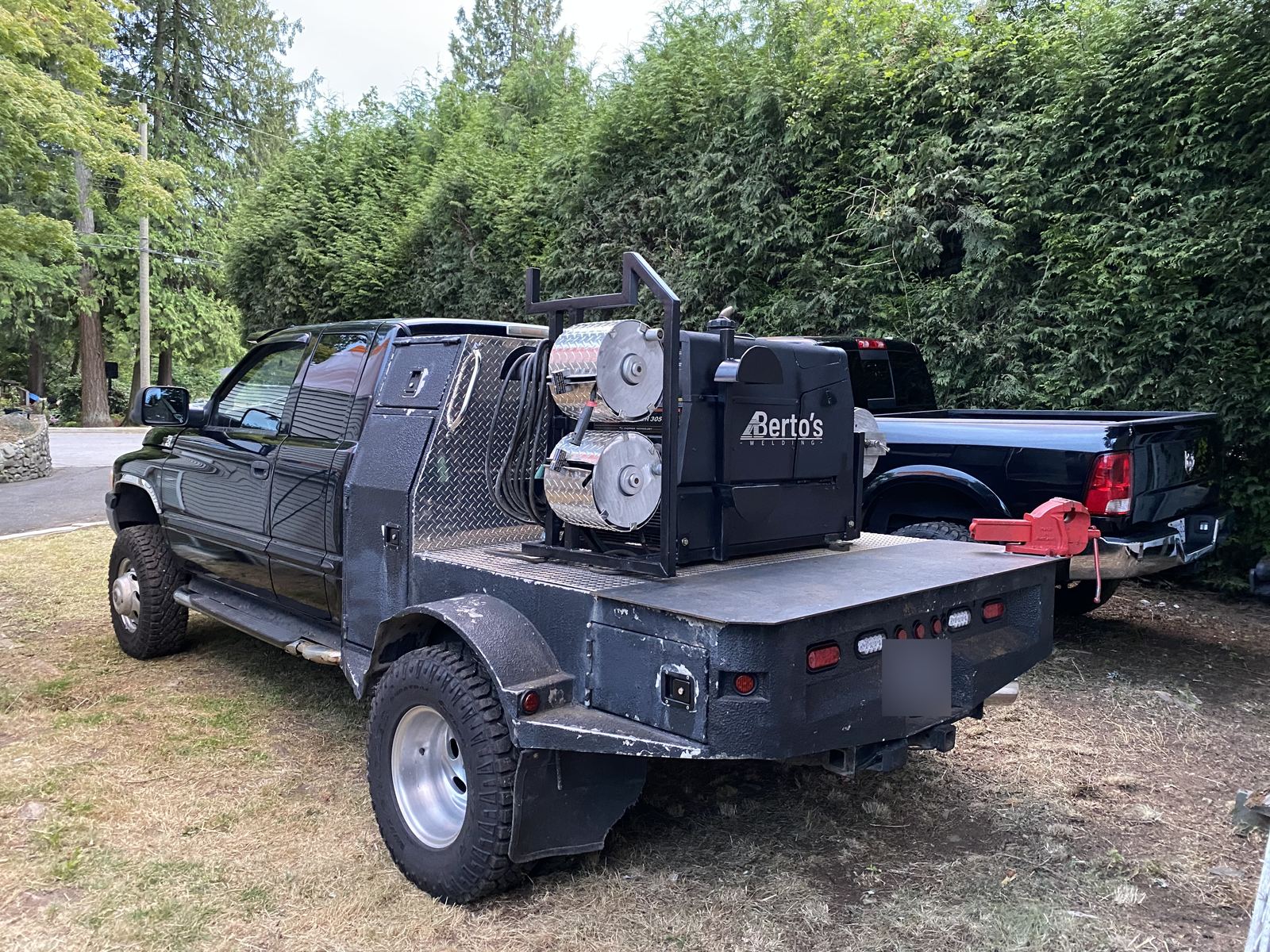 Berto's Welding black flatbed truck with the Berto's-branded welder and two cable reels mounted on the deck, parked on grass