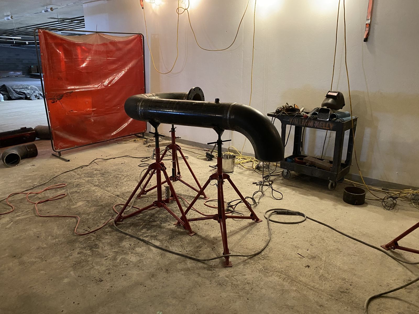 Black steel pipe spool with an elbow set up on red pipe stands, ready for welding