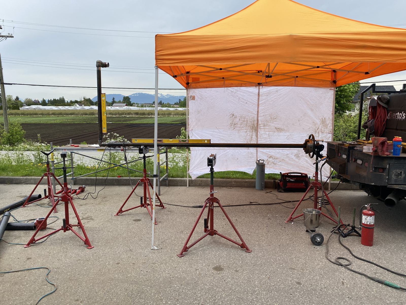 On-site pipe welding setup with pipe on stands under an orange canopy, the welding truck parked alongside