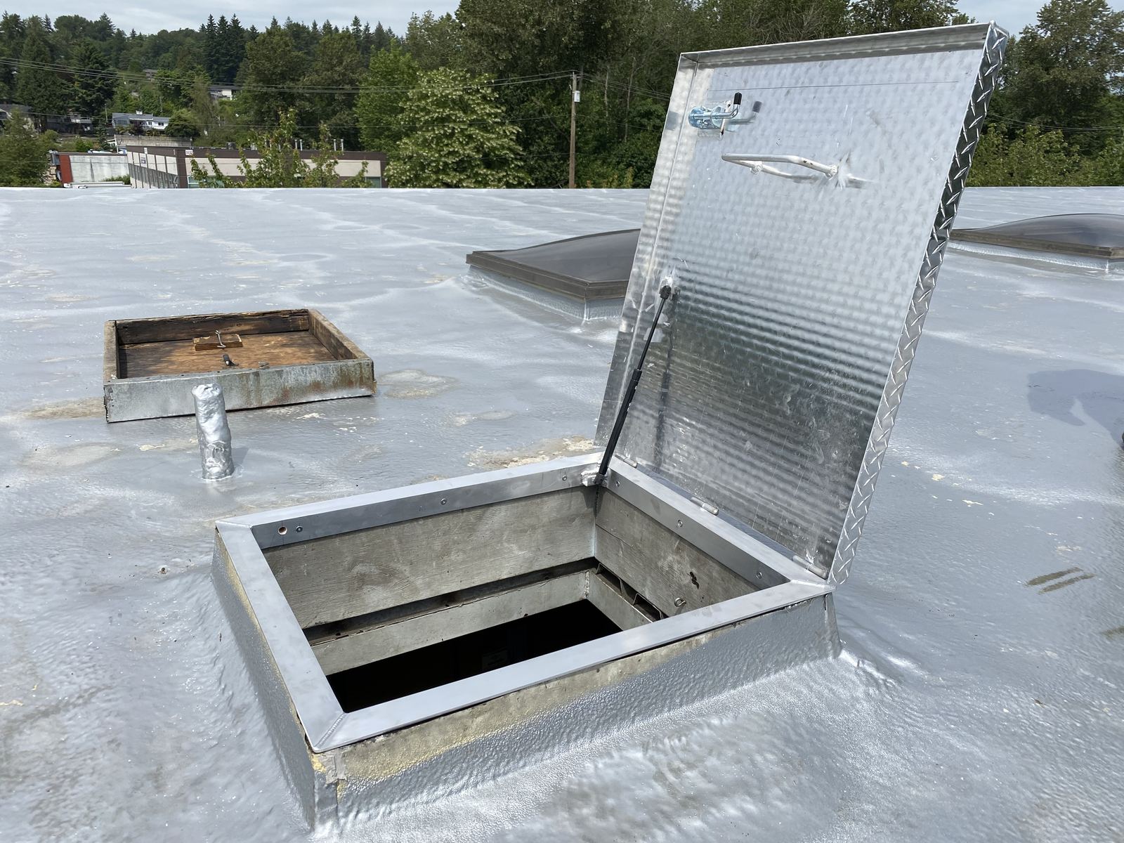 Aluminum diamond-plate roof access hatch standing open on a flat roof