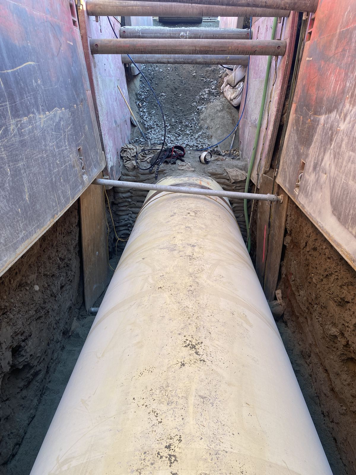 Long run of large wrapped pipe laid in a shored trench, viewed down the line